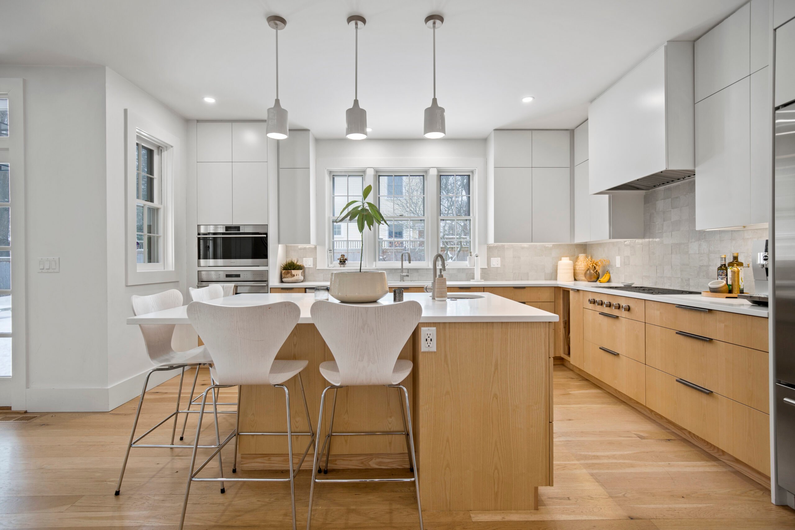Modern kitchen featuring light wood cabinetry, white countertops, and stylish bar stools, designed for showcasing real estate listings effectively.