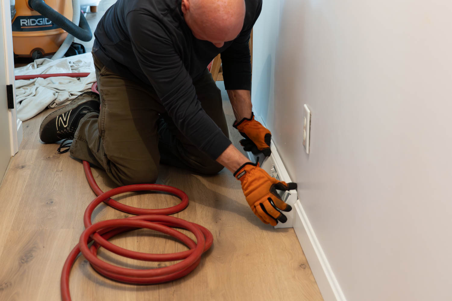 HVAC technician cleaning air ducts with vacuum hose in residential setting, showcasing hands-on service for improved indoor air quality.