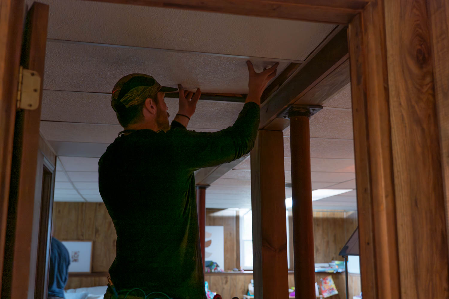 HVAC technician installing ceiling tiles in residential space, showcasing hands-on service and attention to detail in home improvement.