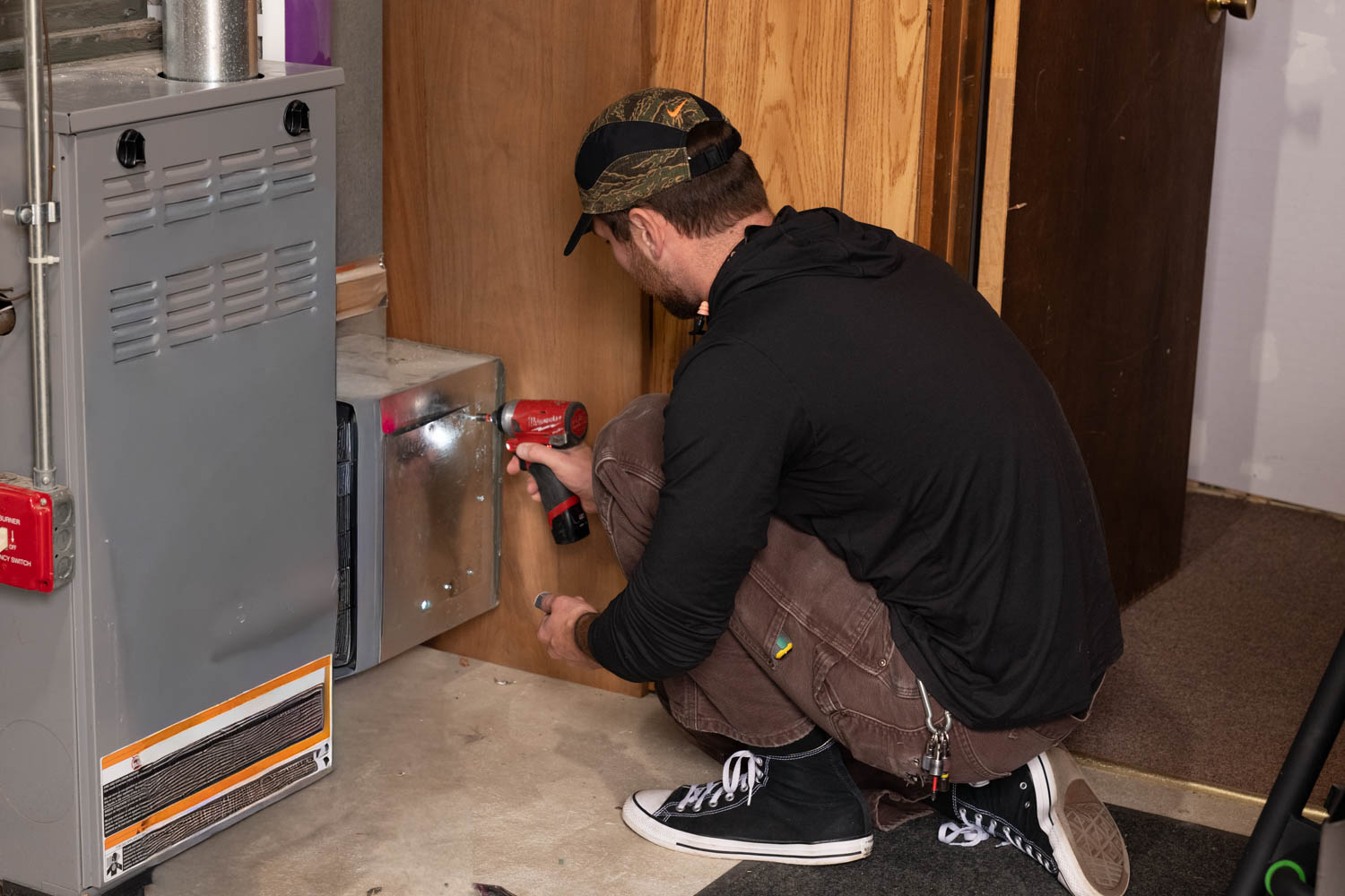 HVAC technician installing equipment using a power drill in a residential setting, showcasing hands-on service for heating and cooling systems.