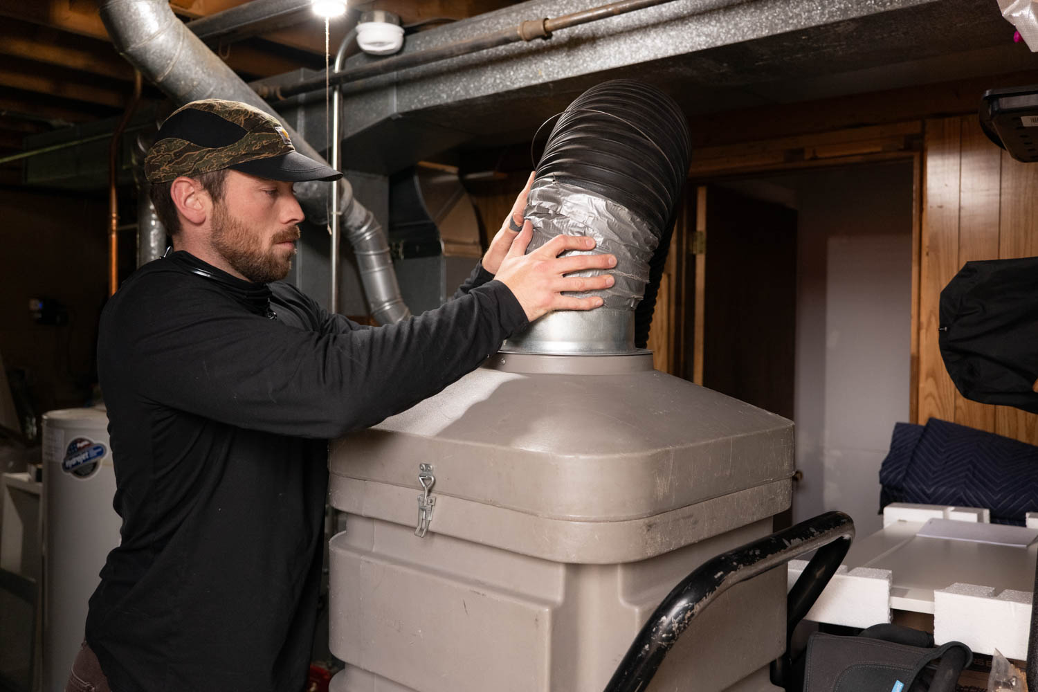 HVAC technician inspecting and securing ductwork on a ventilation system in a residential basement, showcasing hands-on maintenance and repair services.