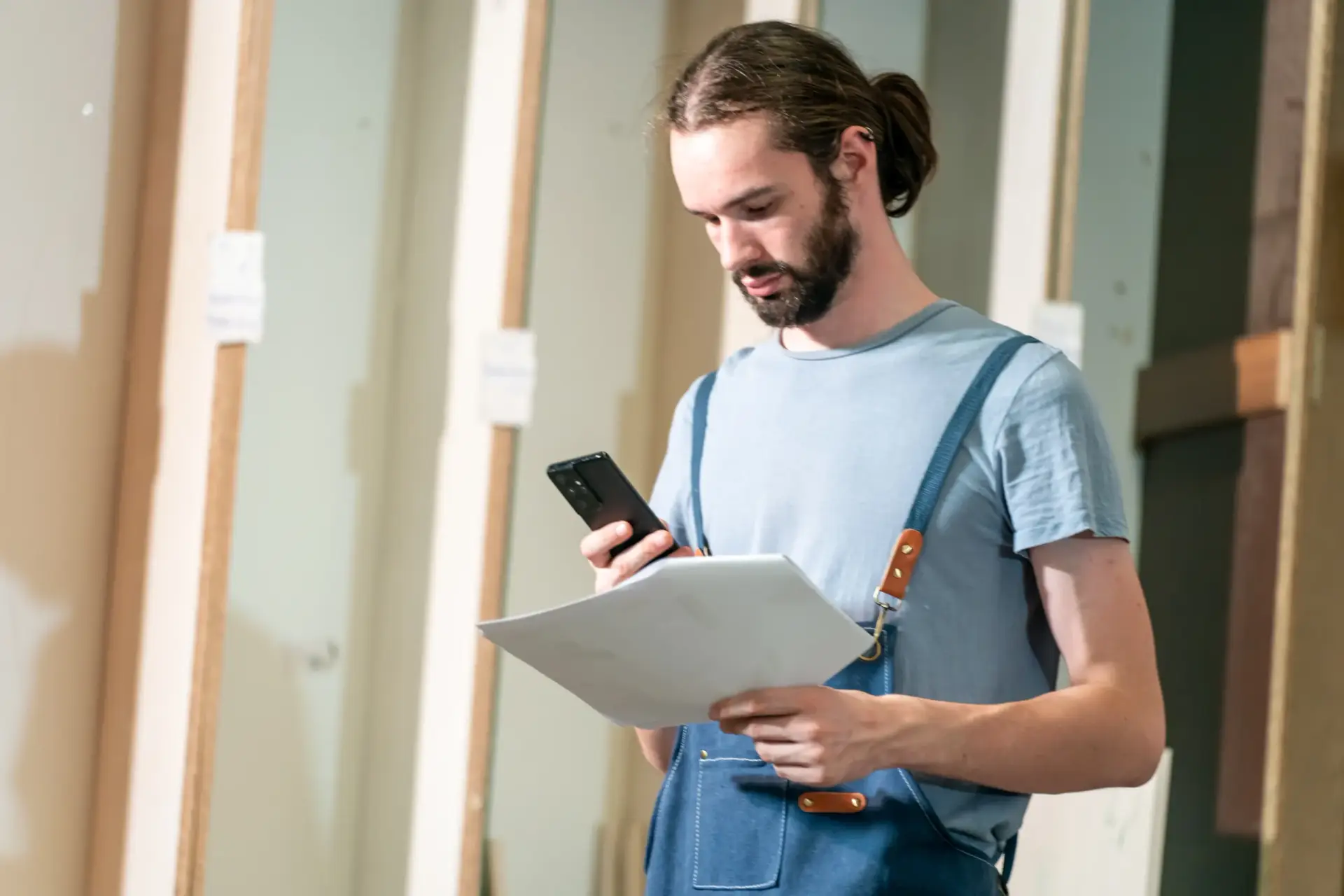 Carpenter reviewing project plans on a smartphone while holding a document in a workshop setting, emphasizing local service strategies for home improvement businesses.