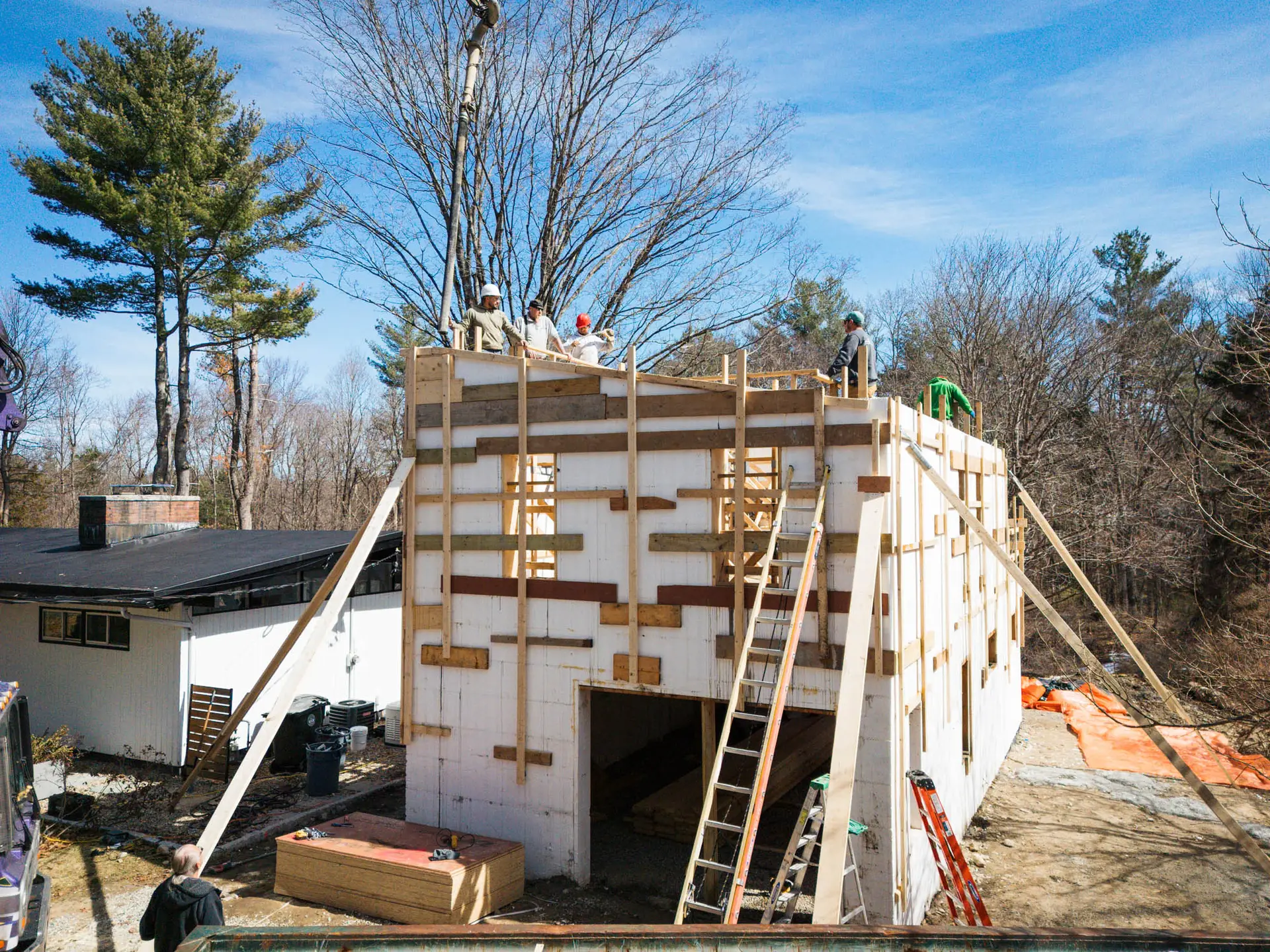 Aerial view of construction workers on site, building a detached ADU with wooden framing and scaffolding, showcasing progress in renovation.