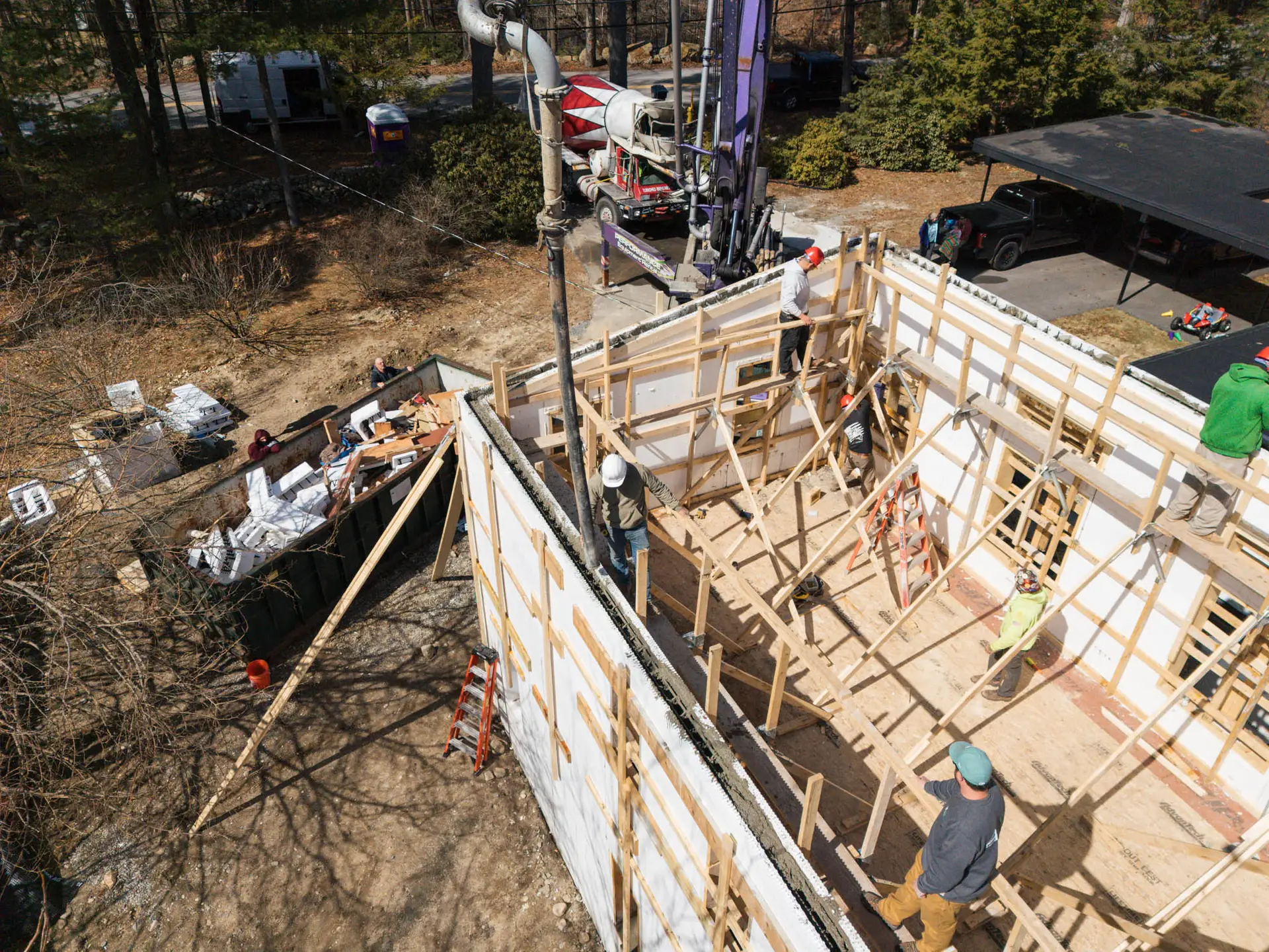 Aerial view of construction site showing workers framing a detached ADU, with concrete pour and materials in the background, illustrating active job progress for Bradford Construction Management.