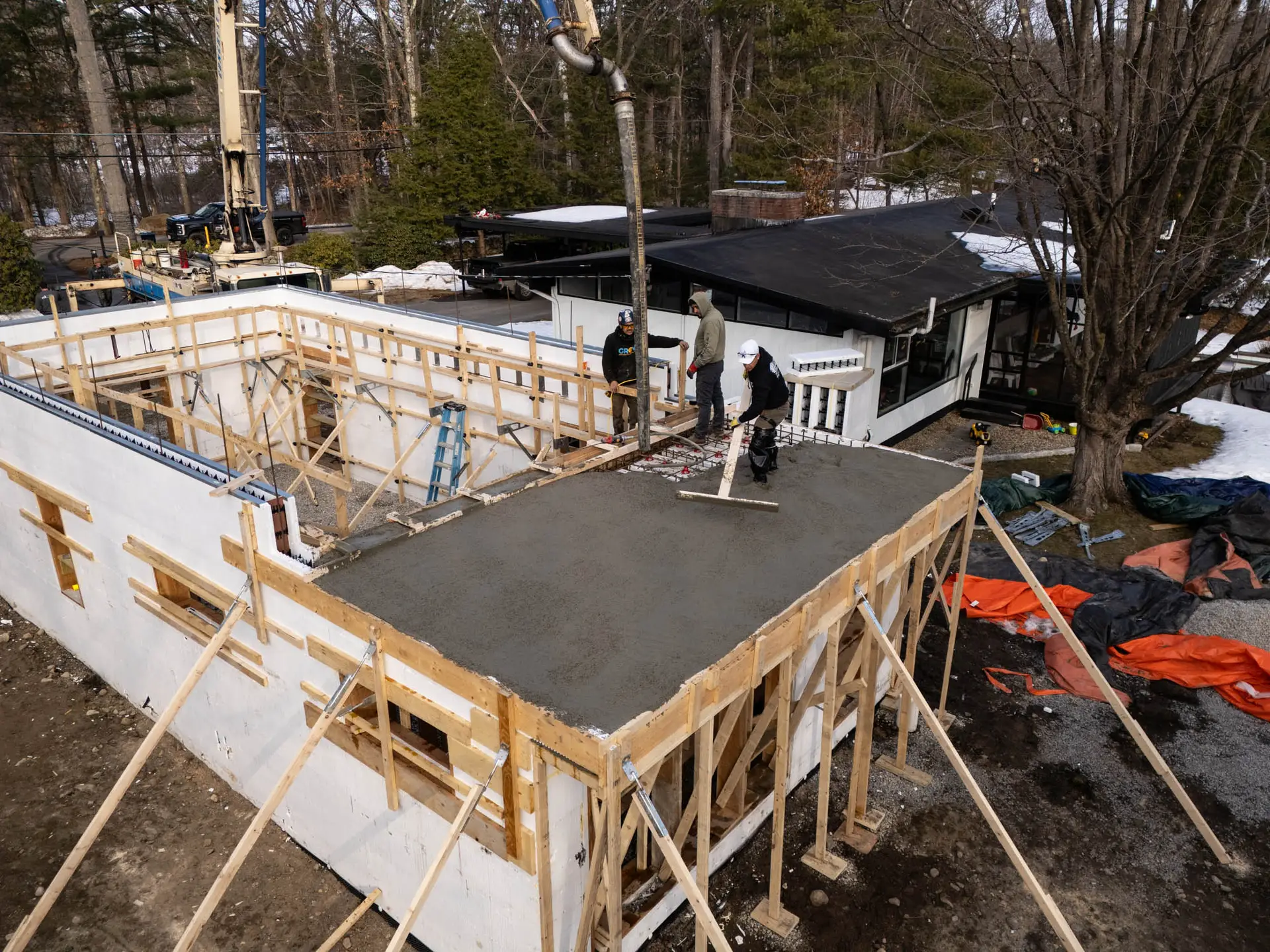 Construction workers pouring concrete on a building foundation, showcasing a remodeling project with scaffolding and tools in a residential area.