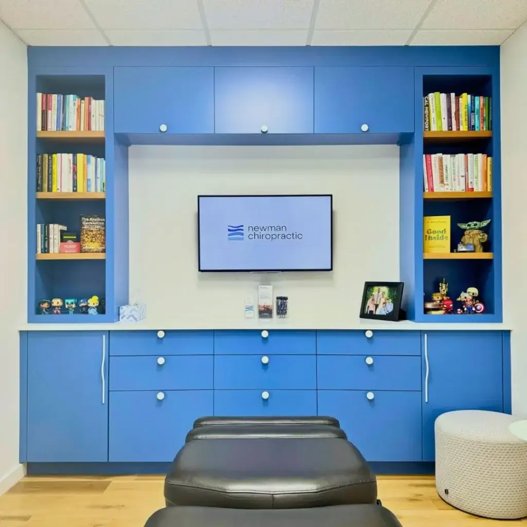 Clinic waiting area with blue built-in cabinetry, bookshelves, and Newman Chiropractic logo on TV.