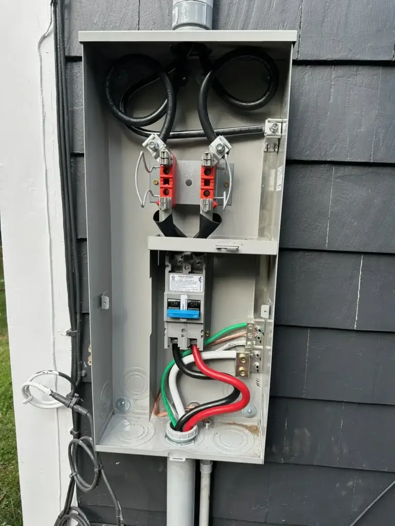 Electrical service panel with wires and connections mounted on a gray wall.